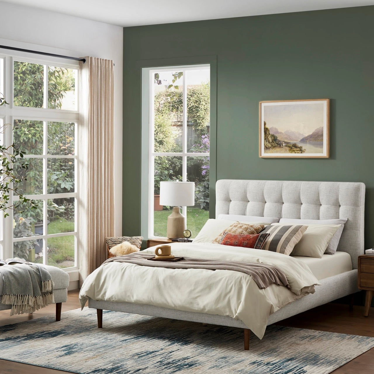 Neatly made bed in a bedroom with green walls, large windows, and decorative pillows.